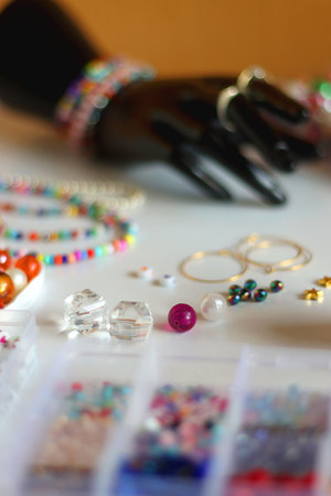 Hand figurine, colorful friendship bracelets, necklaces, various beads and DIY supplies on the table. Making jewelry at home. Selective focus.の写真素材