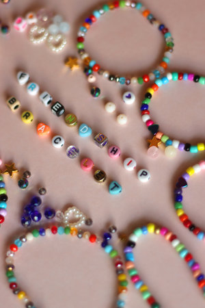 Friendship bracelet spelled with letter beads. Colorful handmade bracelets and various beads. Selective focus, pink background.の写真素材
