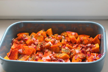 Sheet pan with pieces of butternut squash, onion, herbs and spices. Preparing pumpkin for a roast. Selective focus.の写真素材