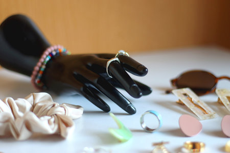 Hand figurine, sunglasses, gold jewelry, colorful bead jewelry, statement rings and various hair accessories on the white table. Selective focus.の写真素材