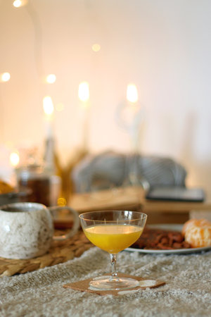 Books, e-reader, tea, orange juice, fruit, snacks, yarn, blanket and lit candles on the table. Autumn or winter hygge at home. Selective focus.の写真素材