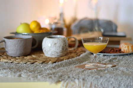 Books, e-reader, tea, orange juice, fruit, snacks, yarn, blanket and lit candles on the table. Autumn or winter hygge at home. Selective focus.の写真素材