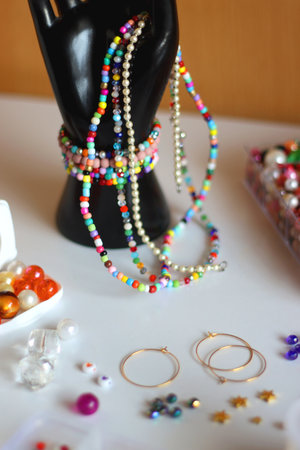 Hand figurine, colorful friendship bracelets, necklaces, various beads and DIY supplies on the table. Making jewelry at home. Selective focus.の写真素材