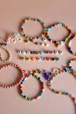 Friendship bracelet spelled with letter beads. Colorful handmade bracelets and various beads. Selective focus, pink background.の写真素材