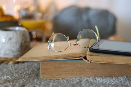 Books, tea, fruit, snacks, yarn, and glasses on the table. Autumn or winter hygge at home. Selective focus.の写真素材