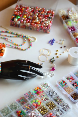 Hand figurine, colorful friendship bracelets, necklaces, various beads and DIY supplies on the table. Making jewelry at home. Selective focus.の写真素材
