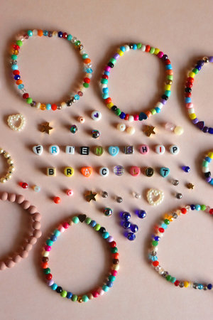 Friendship bracelet spelled with letter beads. Colorful handmade bracelets and various beads. Flat lay, pink background.の写真素材