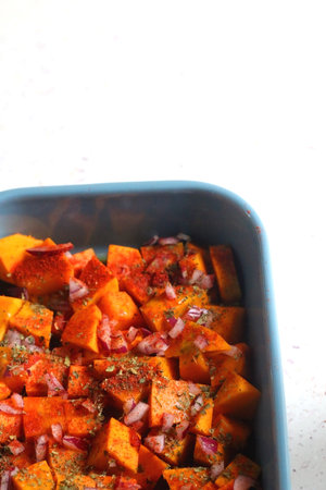 Sheet pan with pieces of butternut squash, onion, herbs and spices. Preparing pumpkin for a roast. Selective focus.の写真素材