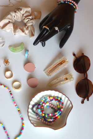 Hand figurine, sunglasses, gold jewelry, colorful bead jewelry, statement rings and various hair accessories on the white table. Selective focus.の写真素材