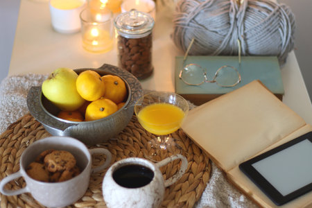 Books, e-reader, tea, orange juice, fruit, snacks, yarn, blanket and lit candles on the table....