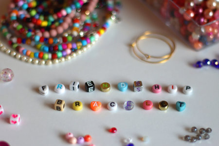 Friendship bracelet spelled with letter beads. Colorful handmade bracelets and various jewelry making supplies. Selective focus, white background.の写真素材