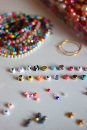 Friendship bracelet spelled with letter beads. Colorful handmade bracelets and various jewelry making supplies. Selective focus, white background.の写真素材