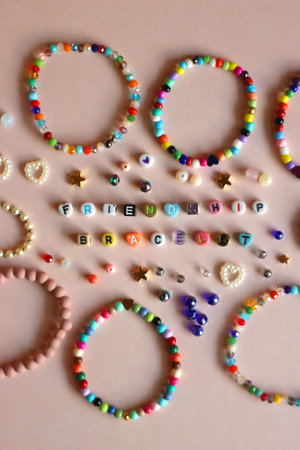 Friendship bracelet spelled with letter beads. Colorful handmade bracelets and various beads. Flat lay, pink background.の写真素材