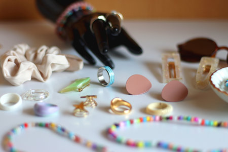 Hand figurine, sunglasses, gold jewelry, colorful bead jewelry, statement rings and various hair accessories on the white table. Selective focus.の写真素材