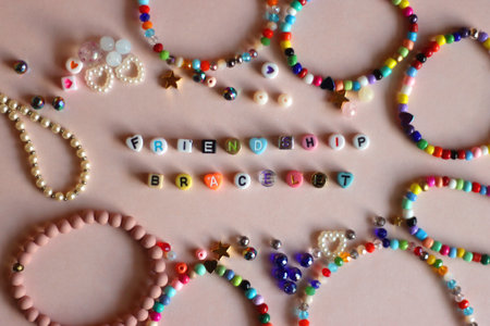 Friendship bracelet spelled with letter beads. Colorful handmade bracelets and various beads. Flat lay, pink background.の写真素材