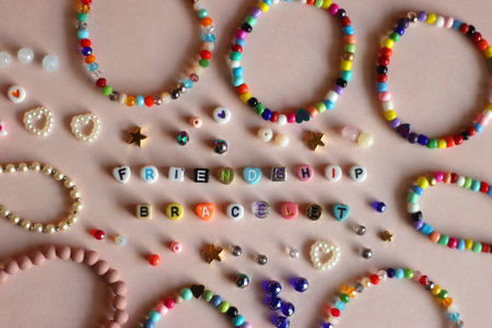 Friendship bracelet spelled with letter beads. Colorful handmade bracelets and various beads. Flat lay, pink background.の写真素材