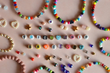 Friendship bracelet spelled with letter beads. Colorful handmade bracelets and various beads. Flat lay, pink background.の写真素材