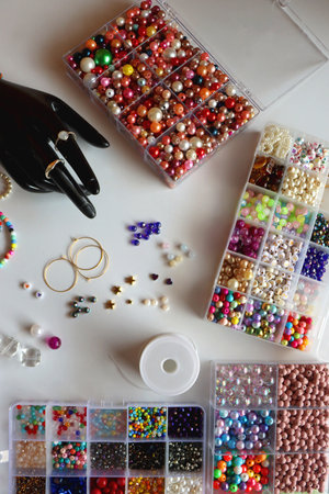 Hand figurine, colorful friendship bracelets, necklaces, various beads and DIY supplies on the table. Making jewelry at home. Flat lay.の写真素材