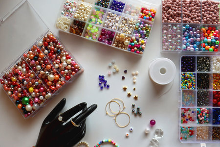 Hand figurine, colorful friendship bracelets, necklaces, various beads and DIY supplies on the table. Making jewelry at home. Flat lay.の写真素材