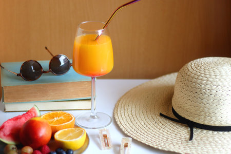 Glass of cocktail, straw hat, sunglasses, books, fresh fruit, chocolate and accessories. Summer essentials on the table. Selective focus.の写真素材