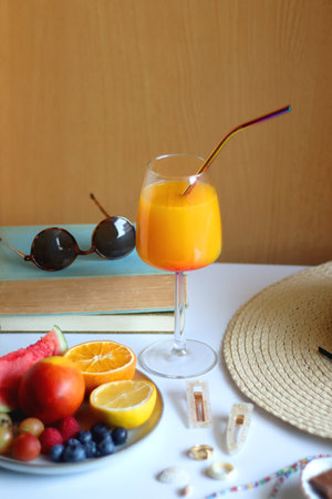 Glass of cocktail, straw hat, sunglasses, books, fresh fruit, chocolate and accessories. Summer essentials on the table. Selective focus.の写真素材