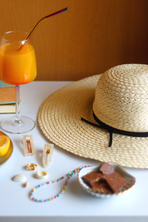 Glass of cocktail, straw hat, sunglasses, books, fresh fruit, chocolate and accessories. Summer essentials on the table. Selective focus.の写真素材