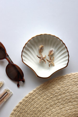 Sunglasses, straw hat, shells and jewelry in neutral colors. Seasonal summer accessories on white background. Flat lay.の写真素材