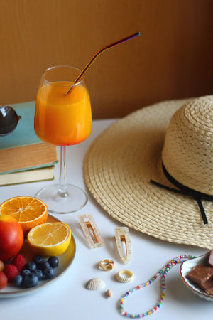Glass of cocktail, straw hat, sunglasses, books, fresh fruit, chocolate and accessories. Summer essentials on the table. Selective focus.の写真素材