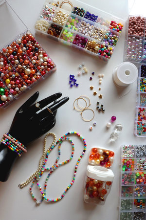 Hand figurine, colorful friendship bracelets, necklaces, various beads and DIY supplies on the table. Making jewelry at home. Flat lay.の写真素材