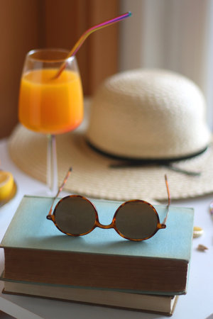 Glass of cocktail, straw hat, sunglasses, books, fresh fruit, chocolate and accessories. Summer essentials on the table. Selective focus.の写真素材