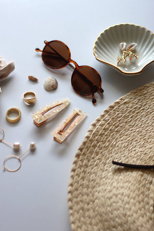 Sunglasses, straw hat, shells and jewelry in neutral colors. Seasonal summer accessories on white background. Selective focus.の写真素材
