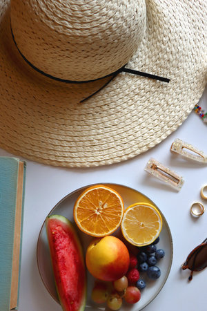 Straw hat, sunglasses, books, fresh fruit, chocolate and accessories. Summer essentials on the table. Top view.の写真素材