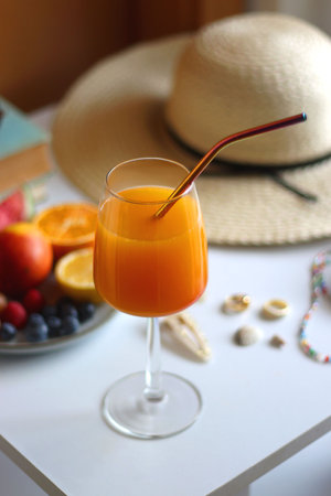 Glass of cocktail, straw hat, sunglasses, books, fresh fruit, chocolate and accessories. Summer essentials on the table. Selective focus.の写真素材