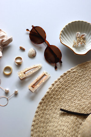 Sunglasses, straw hat, shells and jewelry in neutral colors. Seasonal summer accessories on white background. Selective focus.の写真素材