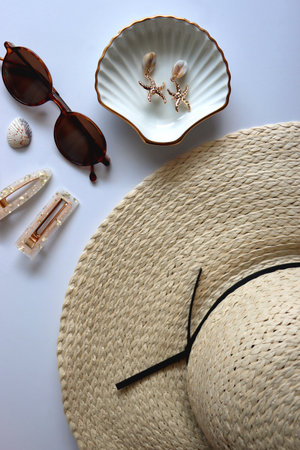 Sunglasses, straw hat, shells and jewelry in neutral colors. Seasonal summer accessories on white background. Flat lay.の写真素材