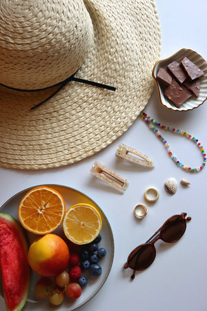 Straw hat, sunglasses, fresh fruit, chocolate and accessories. Summer essentials on the table. Top view.の写真素材