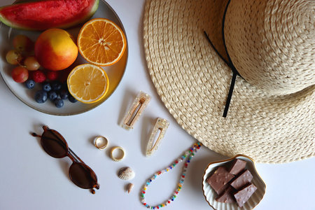 Straw hat, sunglasses, fresh fruit, chocolate and accessories. Summer essentials on the table. Top view.の写真素材