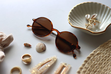 Sunglasses, straw hat, shells and jewelry in neutral colors. Seasonal summer accessories on white background. Selective focus.の写真素材