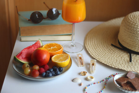 Glass of cocktail, straw hat, sunglasses, books, fresh fruit, chocolate and accessories. Summer essentials on the table. Selective focus.の写真素材