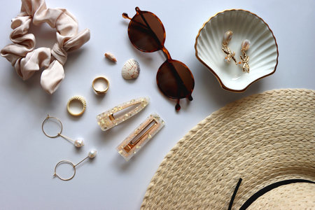 Sunglasses, straw hat, shells and jewelry in neutral colors. Seasonal summer accessories on white background. Flat lay.の写真素材
