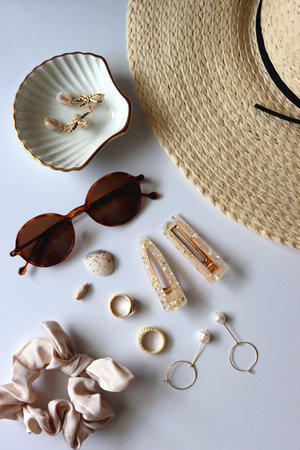 Sunglasses, straw hat, shells and jewelry in neutral colors. Seasonal summer accessories on white background. Flat lay.の写真素材