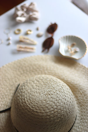 Sunglasses, straw hat, shells and jewelry in neutral colors. Seasonal summer accessories on white background. Selective focus.の写真素材