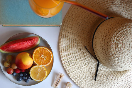 Glass of cocktail, straw hat, sunglasses, books, fresh fruit, chocolate and accessories. Summer essentials on the table. Top view.の写真素材