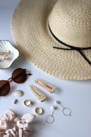 Sunglasses, straw hat, shells and jewelry in neutral colors. Seasonal summer accessories on white background. Selective focus.の写真素材