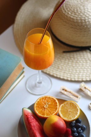 Glass of cocktail, straw hat, sunglasses, books, fresh fruit, chocolate and accessories. Summer essentials on the table. Selective focus.の写真素材