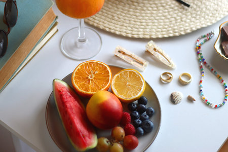 Glass of cocktail, straw hat, sunglasses, books, fresh fruit, chocolate and accessories. Summer essentials on the table. Selective focus.の写真素材