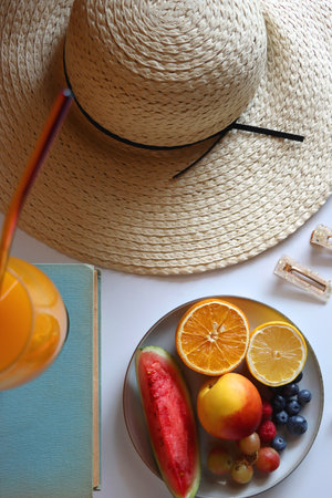 Glass of juice, straw hat, books, fresh fruit, chocolate and accessories. Summer essentials on the table. Top view.の写真素材