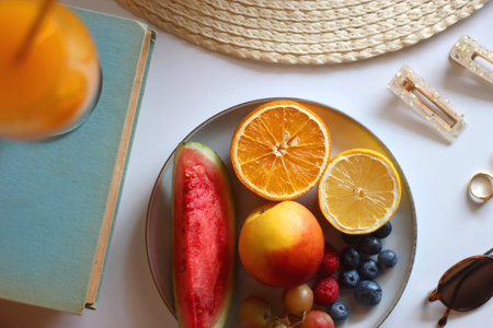Glass of cocktail, straw hat, sunglasses, books, fresh fruit, and accessories. Summer essentials on...