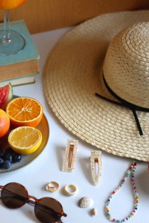 Glass of cocktail, straw hat, sunglasses, books, fresh fruit, chocolate and accessories. Summer essentials on the table. Selective focus.の写真素材
