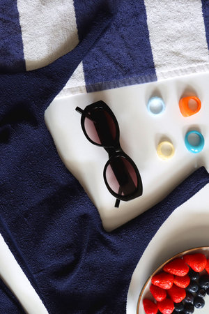 Navy swimsuit, striped beach towel, sunglasses, colorful rings and plate with berries. Top view.の写真素材